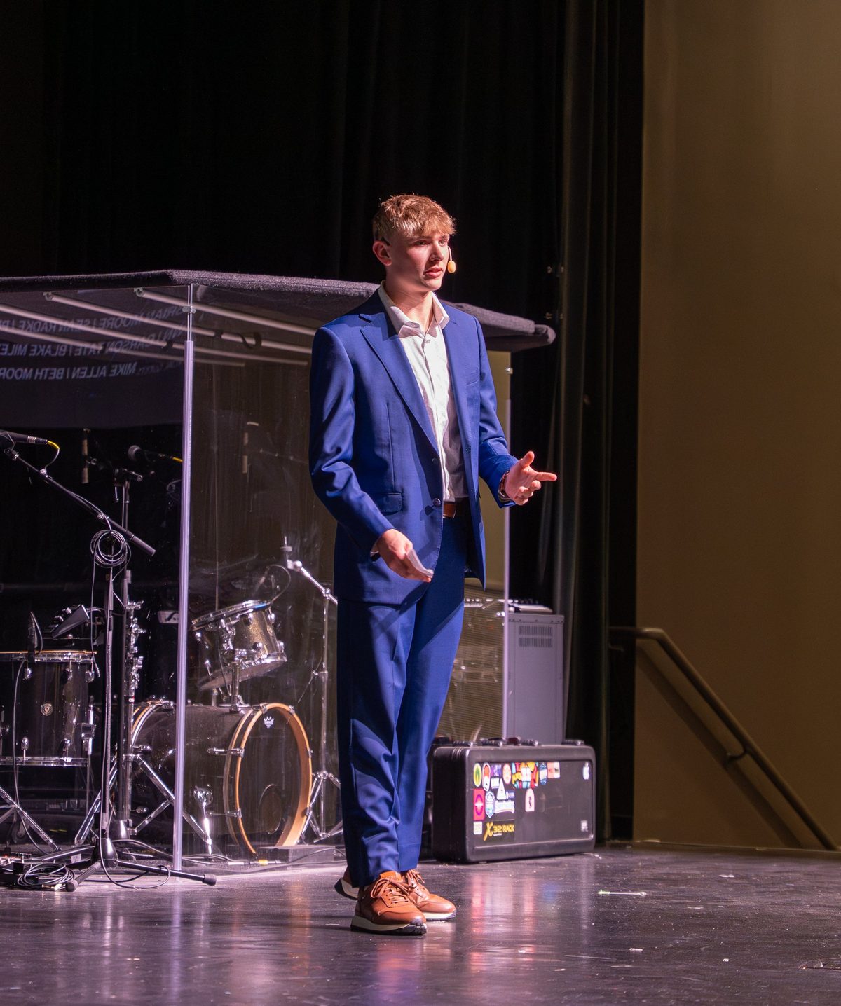 Isaac Shoener speaking on stage in a blue suit
